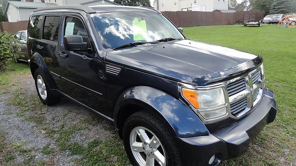 Black SUV parked on gravel near a grassy field and houses