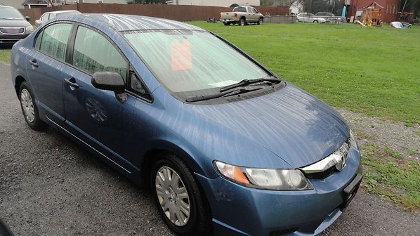 Blue sedan parked on a wet grassy roadside under overcast skies.