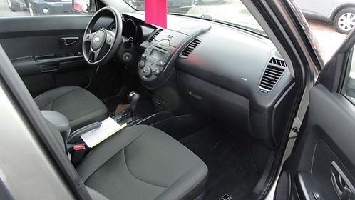 Car interior with black seats, dashboard, and open driver’s door, viewed from the passenger side