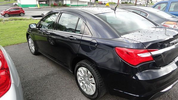 Black sedan parked on a wet lot, rear side view with other cars nearby