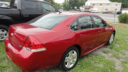 Red sedan parked on grass beside a black pickup truck in a lot