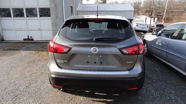 Rear view of a gray Nissan SUV parked outdoors beside a silver car near a garage.