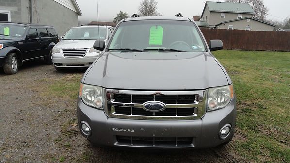 Front view of a silver Ford SUV parked on gravel in a residential driveway, with a green sale sign on the windshield