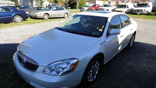 White sedan parked outdoors on a sunny day, with other cars in the background.