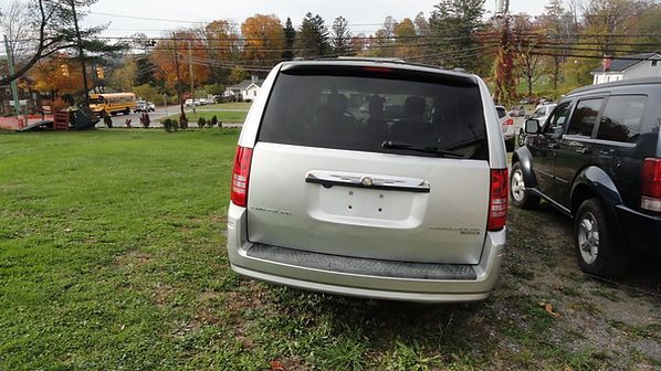 Silver van parked on grass at an outdoor lot, rear view with autumn trees in the background