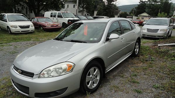 Silver sedan parked in a gravel lot with several other cars in the background.