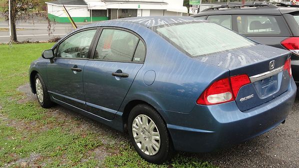 Blue sedan parked on grass beside another car in a parking lot