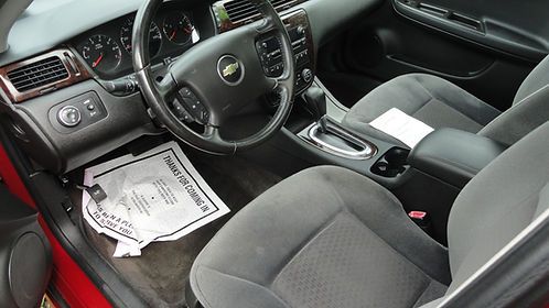 Car interior with black seats, steering wheel, center console, and papers on the front passenger floor.