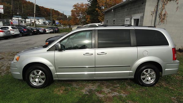 Silver minivan parked on grass beside a car lot, side view.