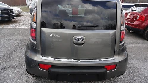 Rear view of a gray Kia Soul parked in a lot, with red cars on either side.