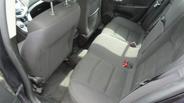 Gray car back seat with folded front seats and red seatbelt buckles visible.