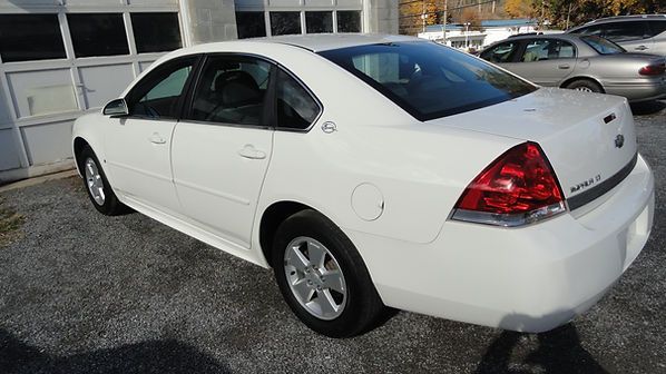 White sedan parked in a lot, rear three-quarter view on a sunny day