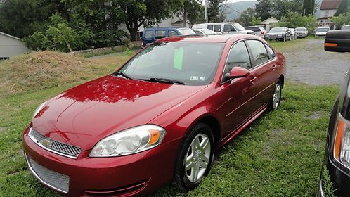 Red sedan parked on grass at a car lot, front-left view.
