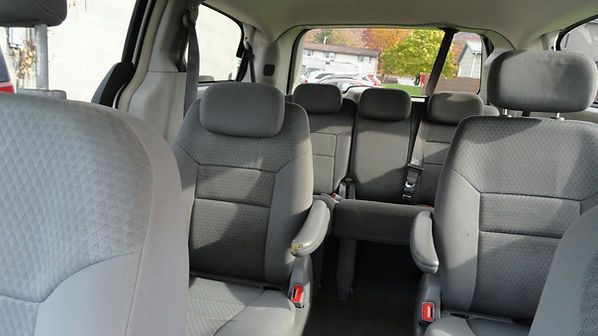 Interior of a gray minivan with three rows of seats and child car seats in the back.
