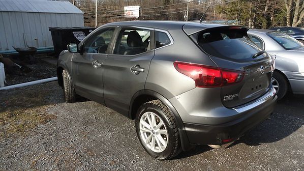 Gray SUV parked on gravel beside a barn in a rural lot, rear three-quarter view