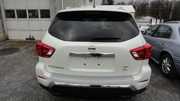 Rear view of a white Nissan SUV parked on wet pavement beside a silver car and garage doors