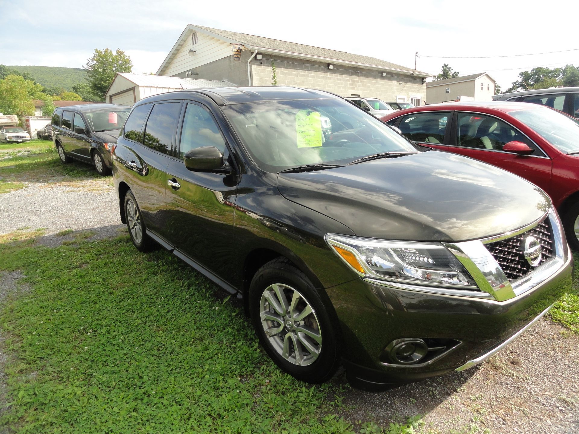 2015 Nissan Pathfinder 4WD parked on grass beside a red car in a lot, front three-quarter view