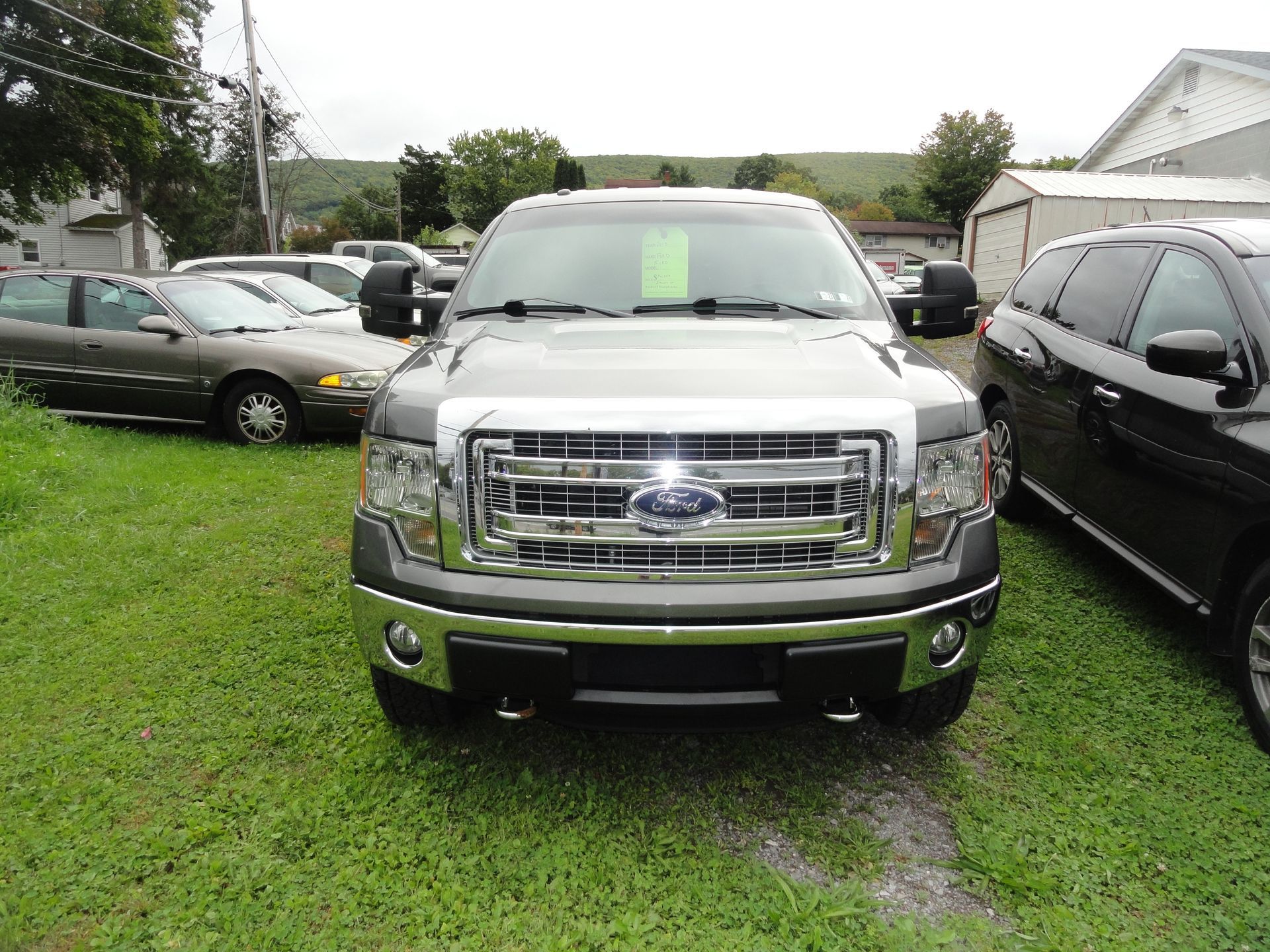 Front view of a silver Ford pickup parked on grass between two cars in a lot.