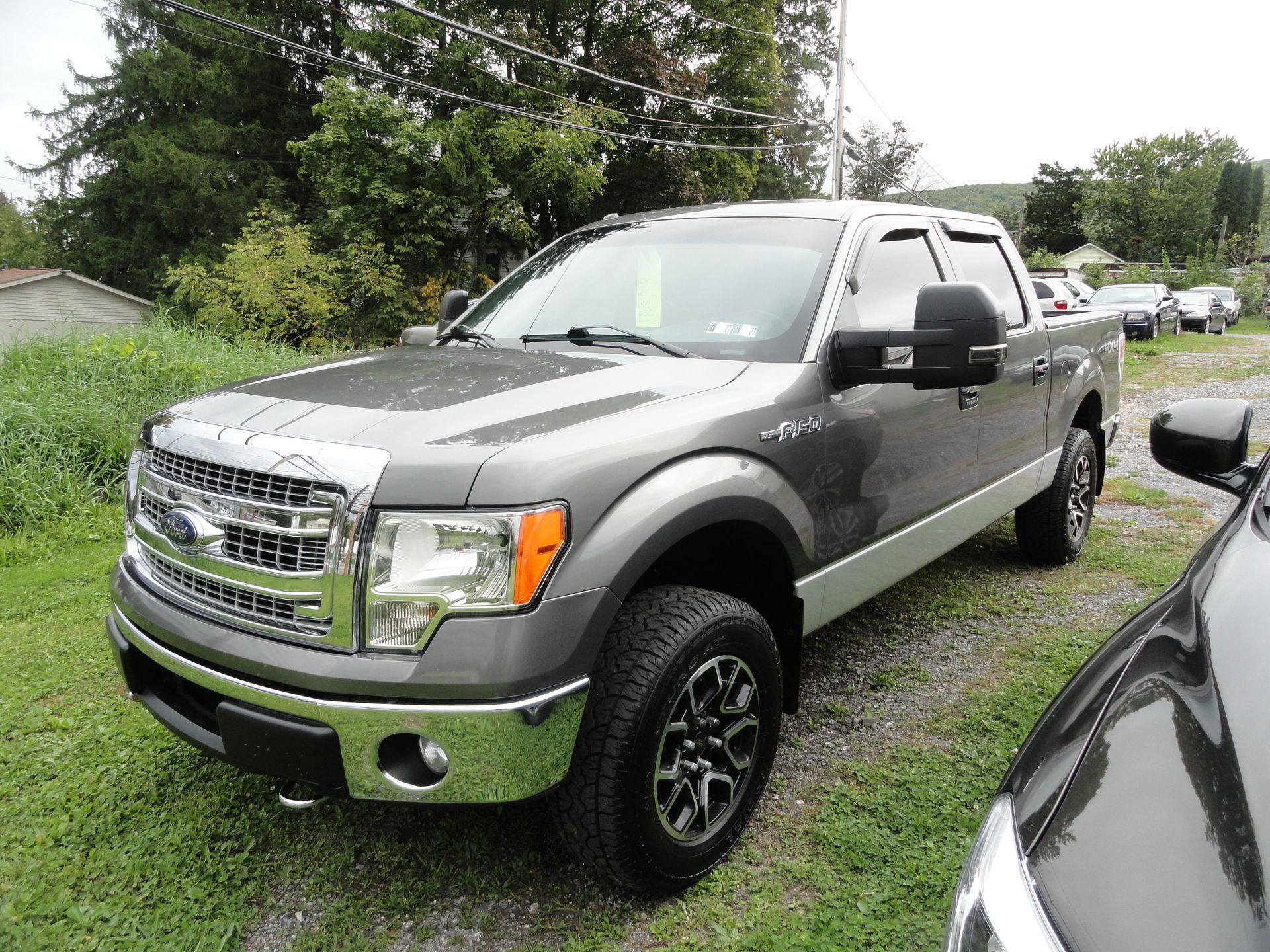 Gray Ford pickup truck parked on a gravel roadside beside trees and grass