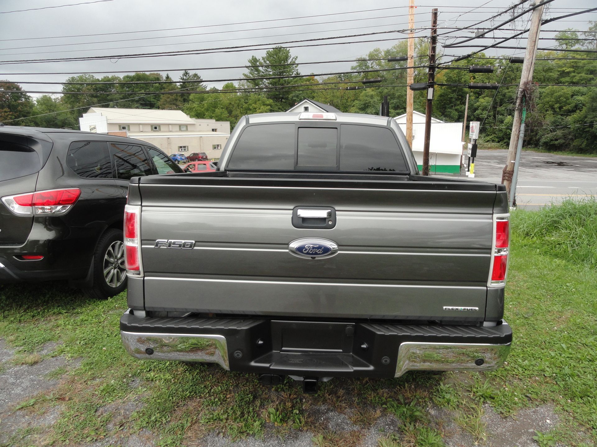 Gray pickup truck parked on a grassy lot, rear view with trailer hitch visible