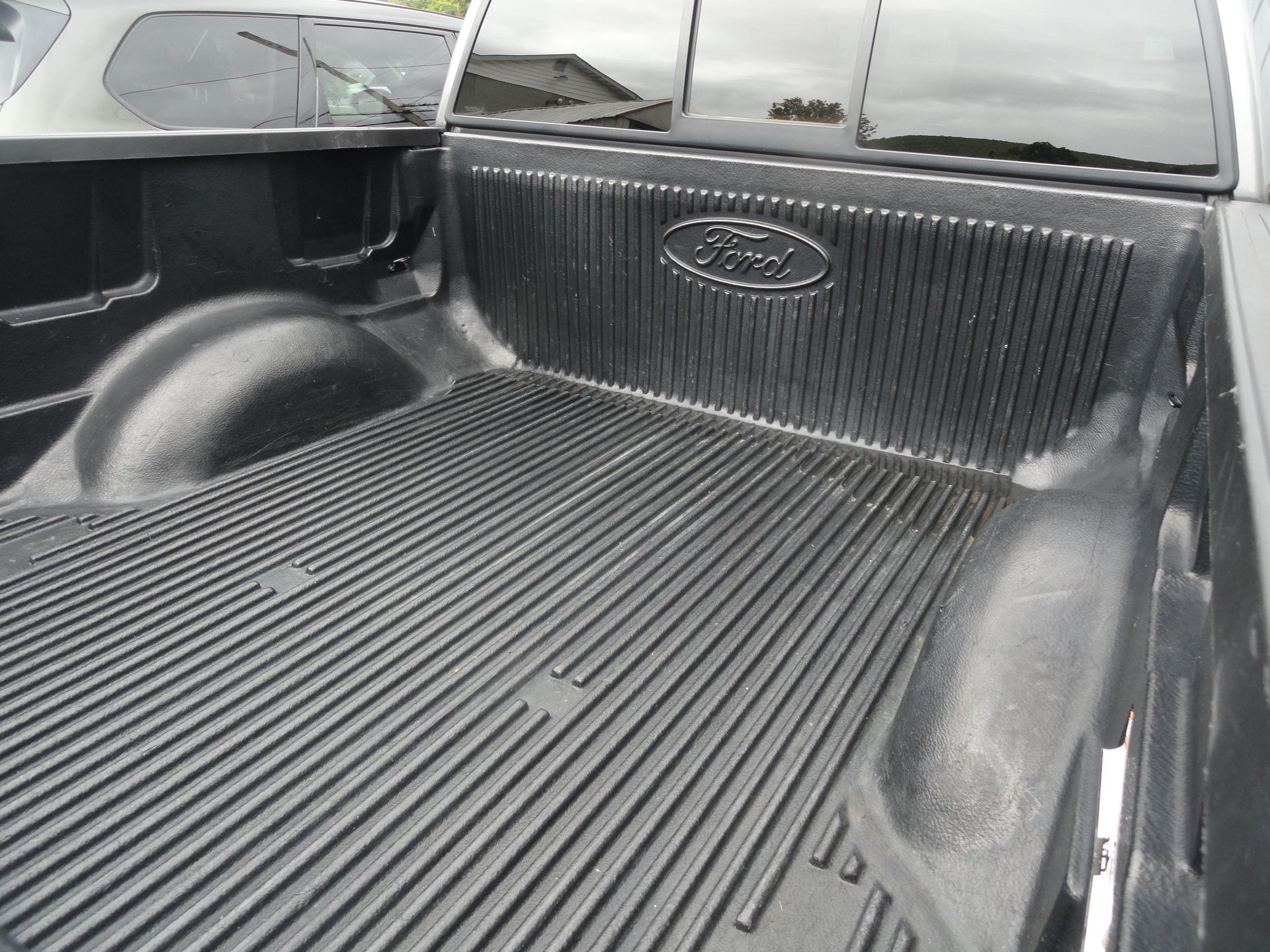 Empty black Ford pickup truck bed with ribbed liner and tailgate window visible