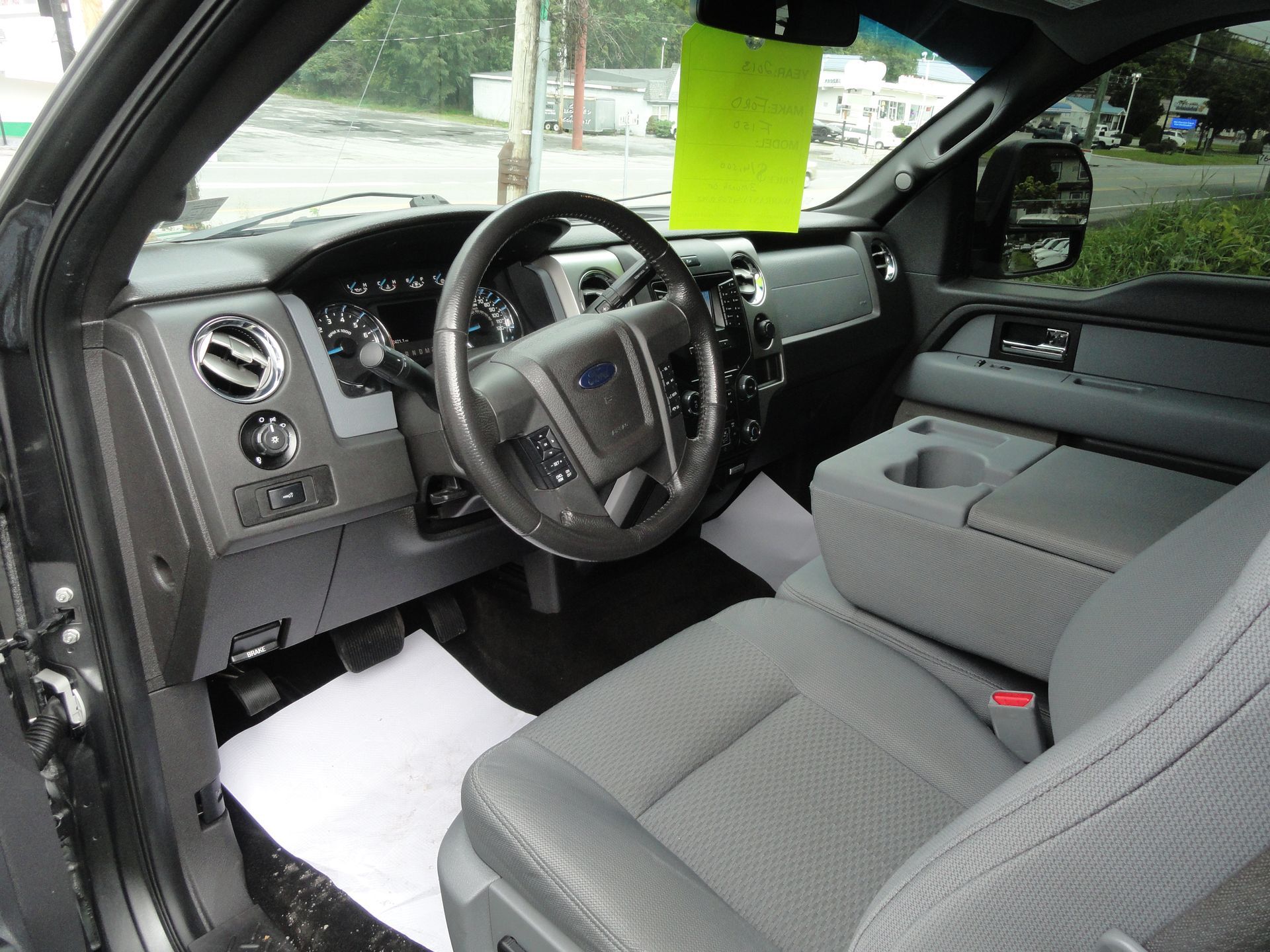 Car interior with gray seats and dashboard, steering wheel, and a bright green tag hanging from the rearview mirror