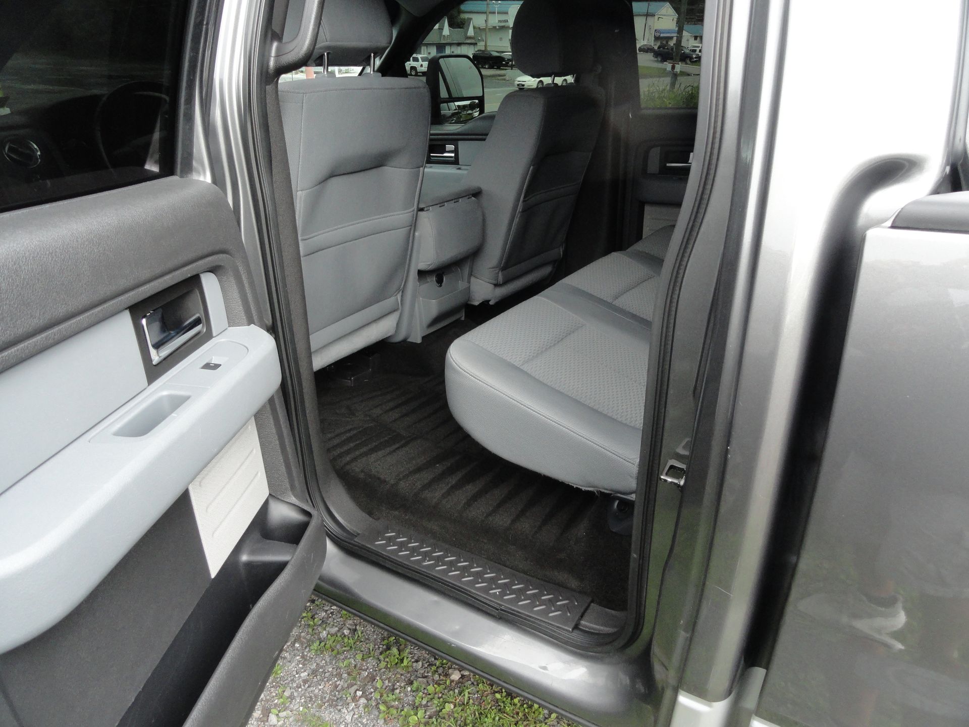 Open car door showing the back seat, gray upholstery, and black floor mat.