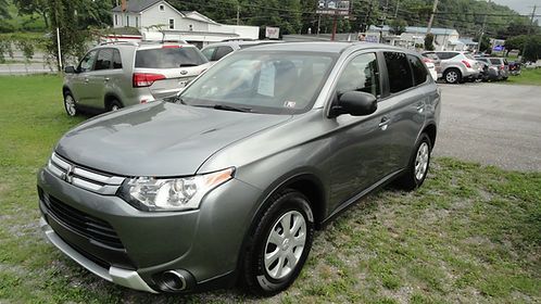Gray SUV parked on grass in a lot, with other cars and houses in the background.