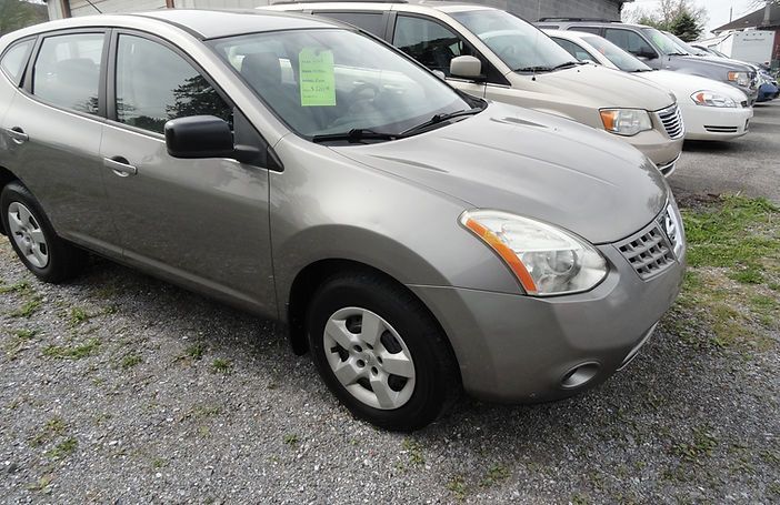 Gray sedan parked on a gravel lot with other cars in the background