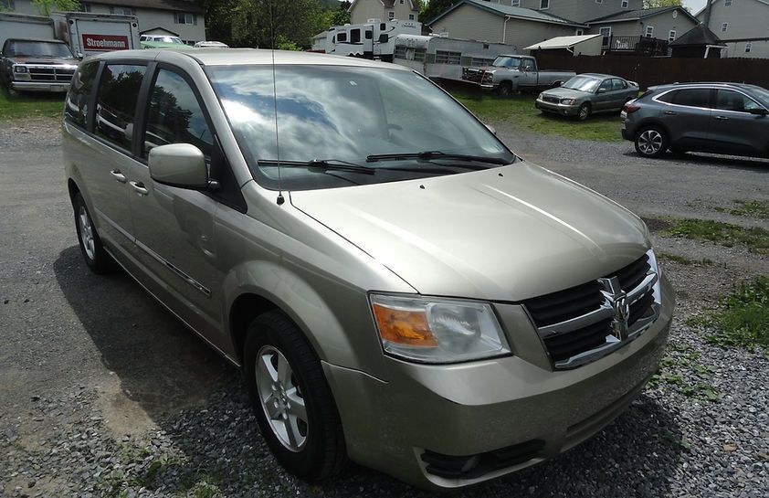 Beige Dodge minivan parked in a gravel lot with houses in the background