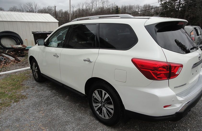 White SUV parked on a gravel driveway beside a barn on an overcast day
