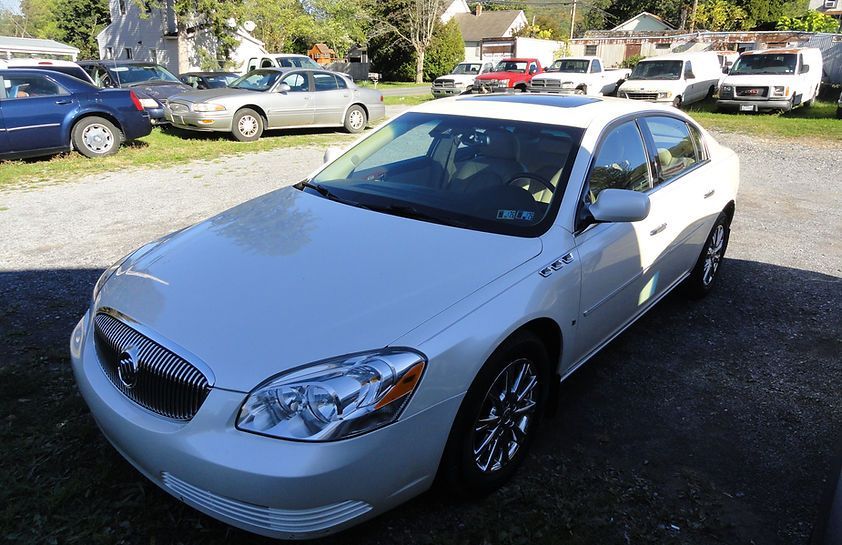 White sedan parked outdoors in a sunny lot with other cars in the background