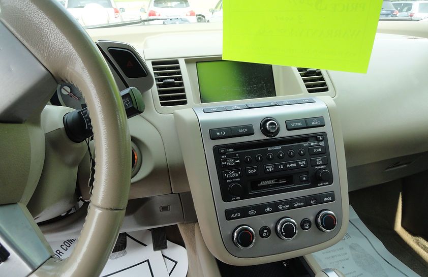 Car dashboard with steering wheel, center console controls, and a bright green note on the windshield.