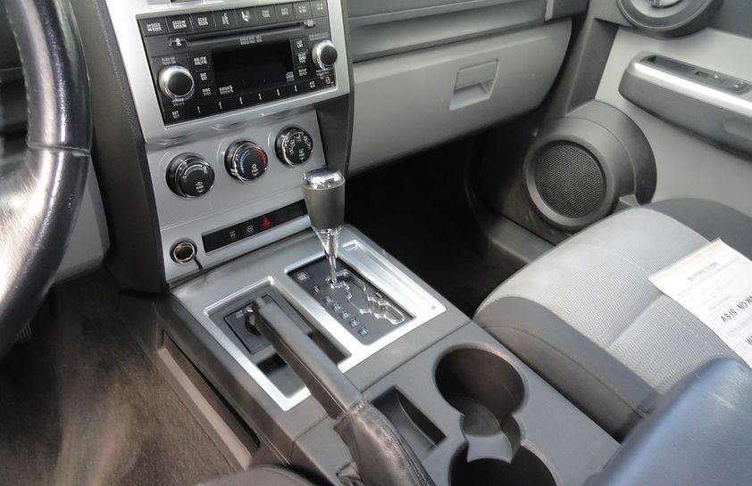 Car interior showing center console, gear shift, cupholders, radio, and gray passenger seat.