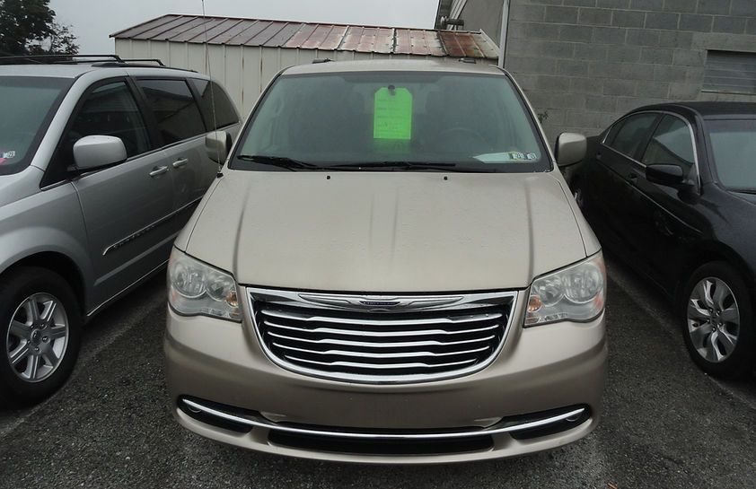 Front view of a beige minivan parked between two cars, with a green sign in the windshield.