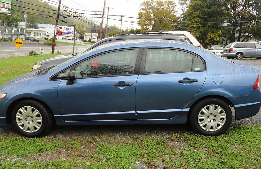 Blue sedan parked on a grassy roadside under overcast skies
