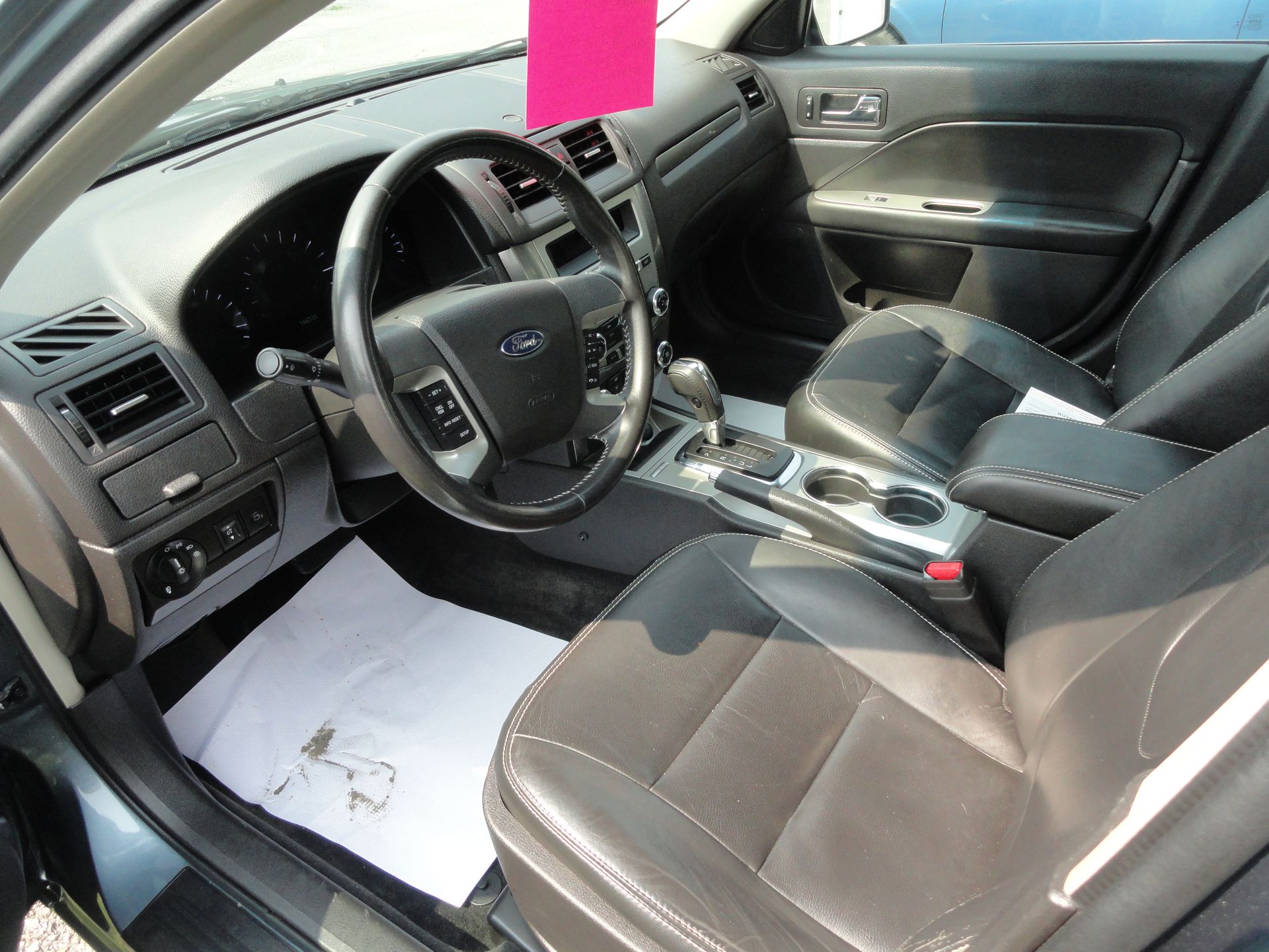 Car interior with black seats, steering wheel, center console, and a bright pink hanging tag.