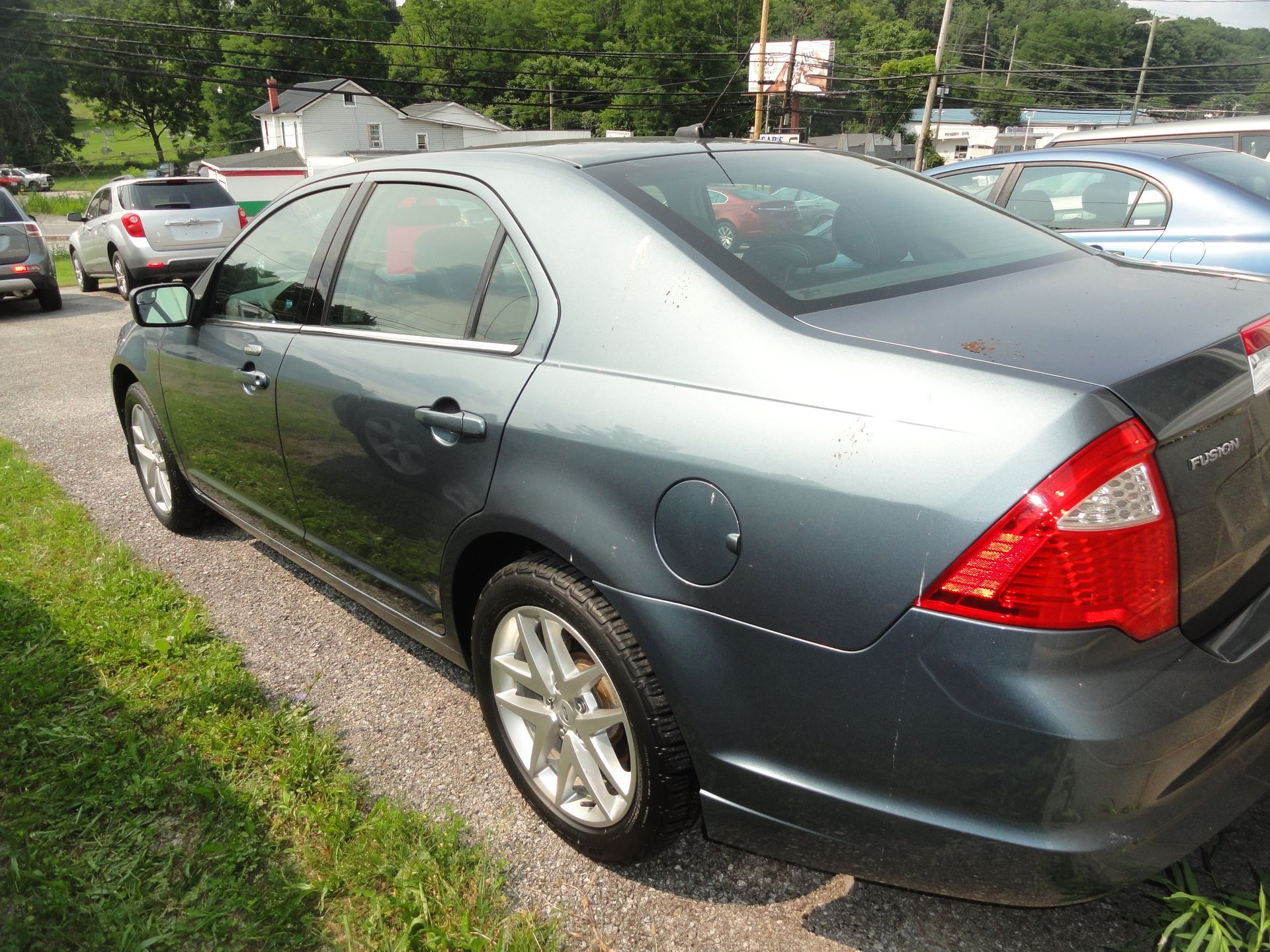 Gray sedan parked on grass beside other cars in a roadside lot