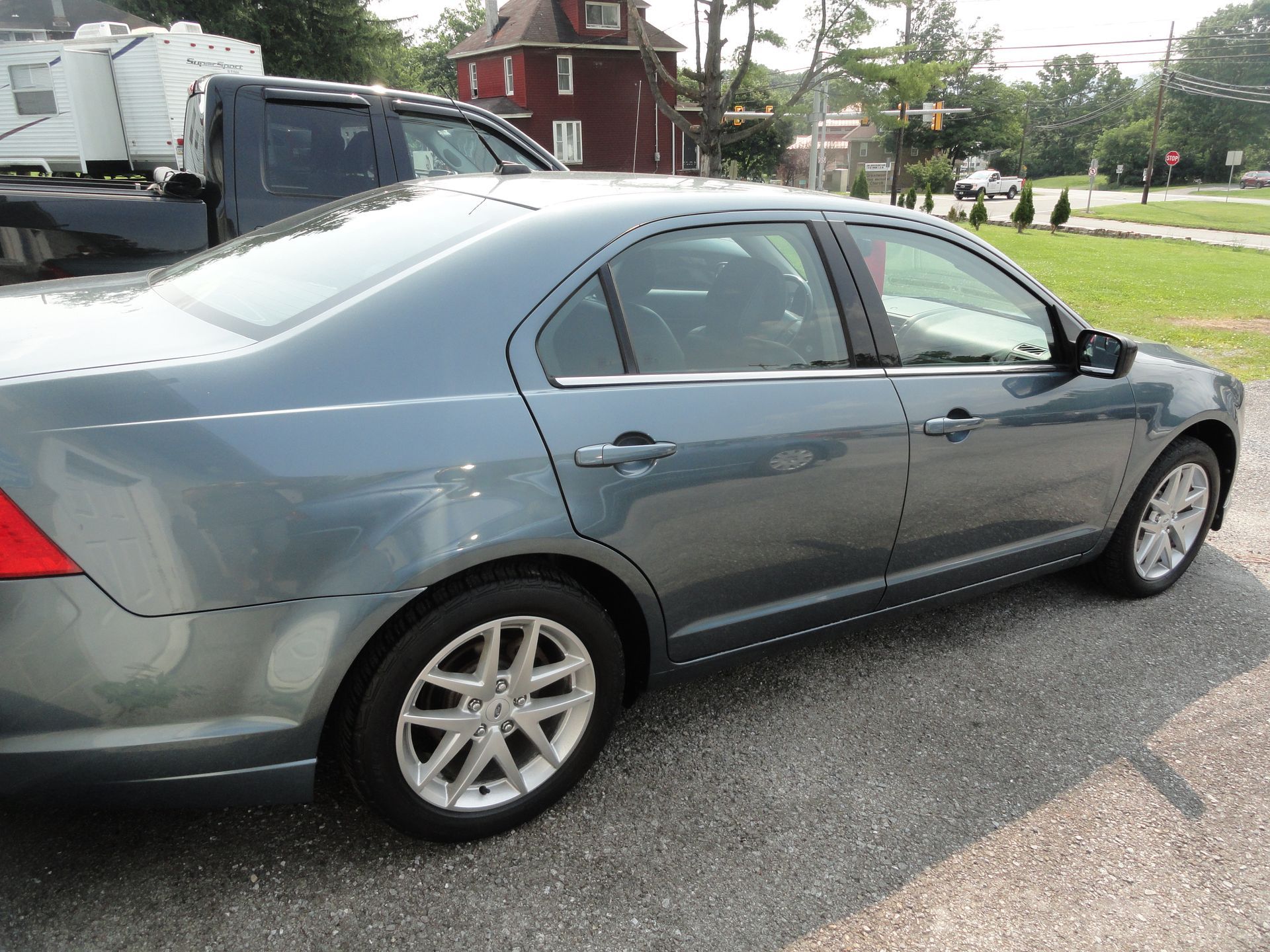 Gray sedan parked on a wet street beside a grassy park and houses