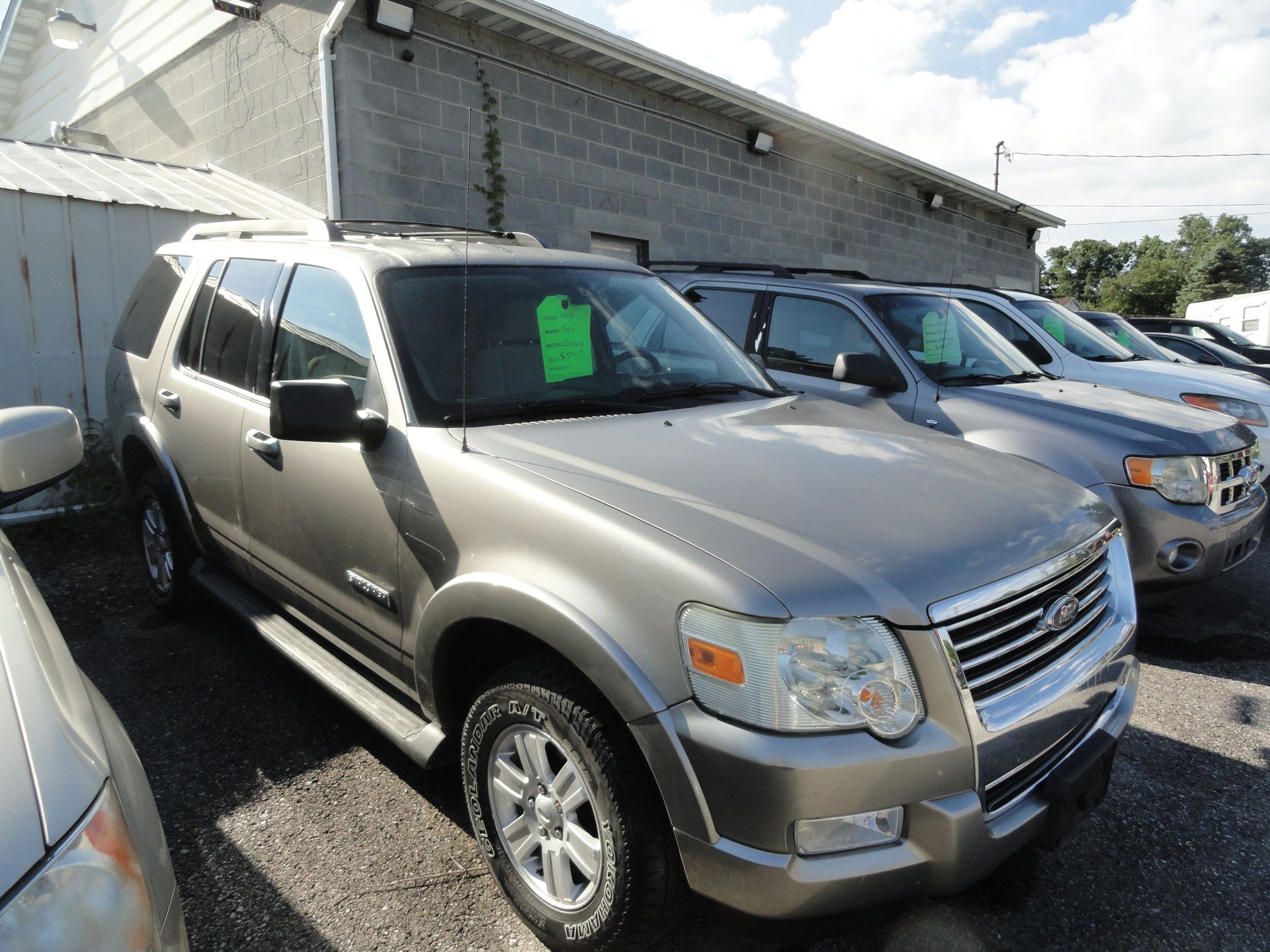 Silver SUV parked in a lot beside other vehicles, with a bright green sale sign in the windshield
