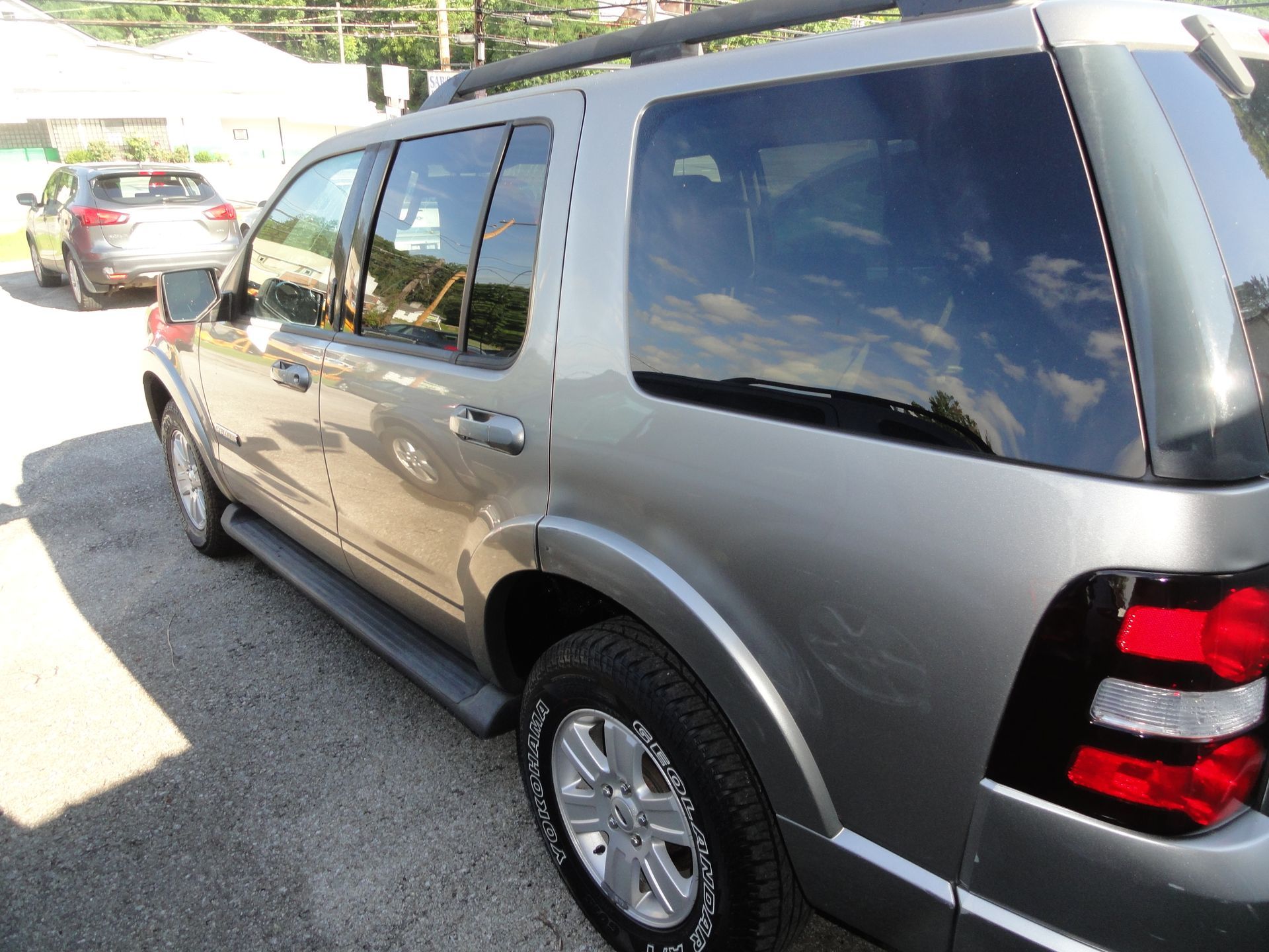 Silver SUV parked in a driveway, rear-side view with other cars and a bright sky reflected in the windows