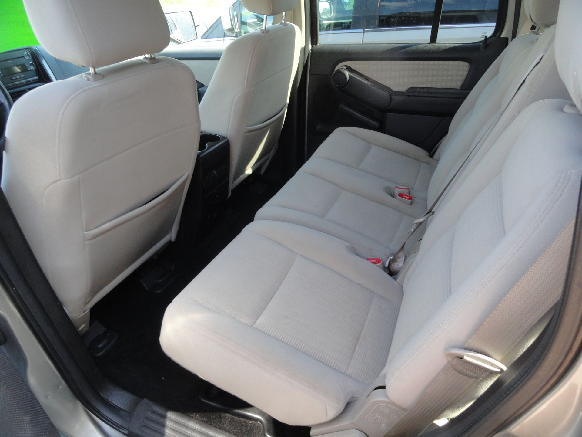 Back seat of a SUV with beige upholstery and black floor mats, viewed from the open rear door