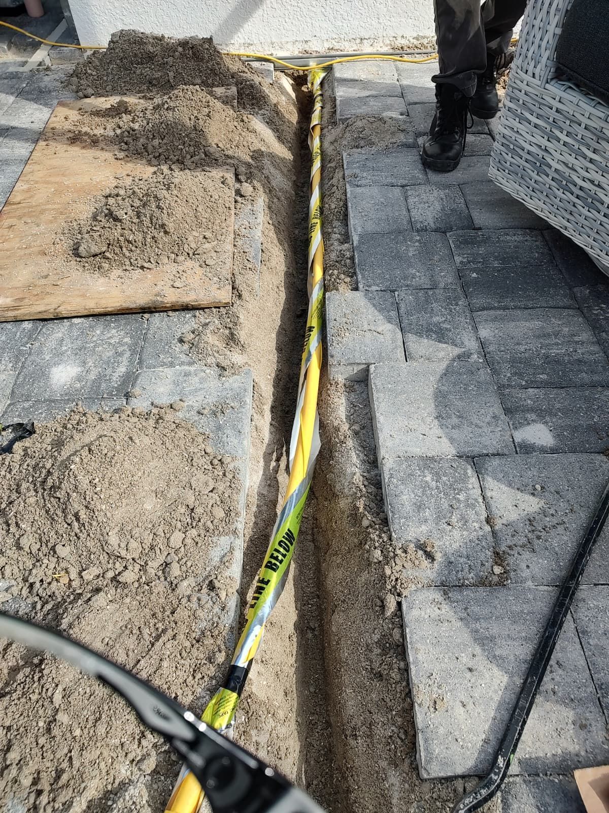 Trench with yellow cables being laid, next to a brick patio.