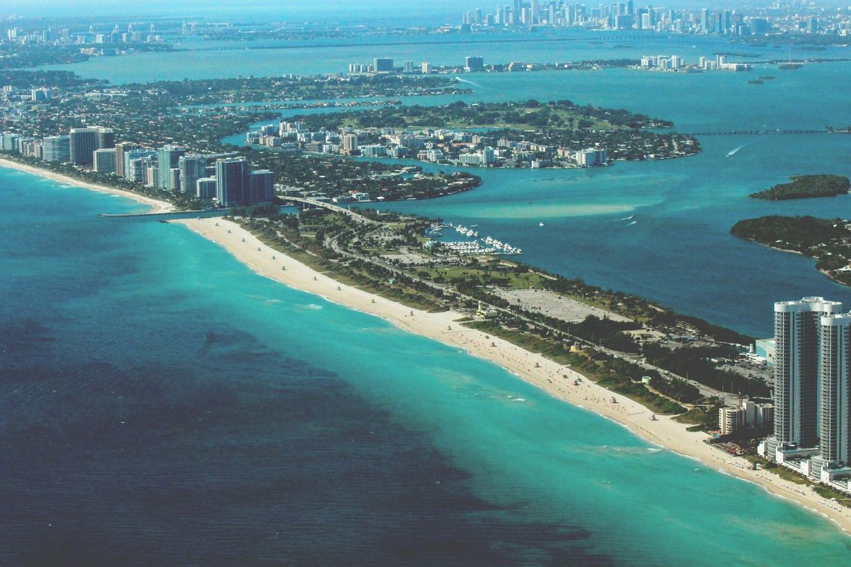 Aerial view of Miami Beach: turquoise water, white sandy beach, high-rise buildings, and city skyline.