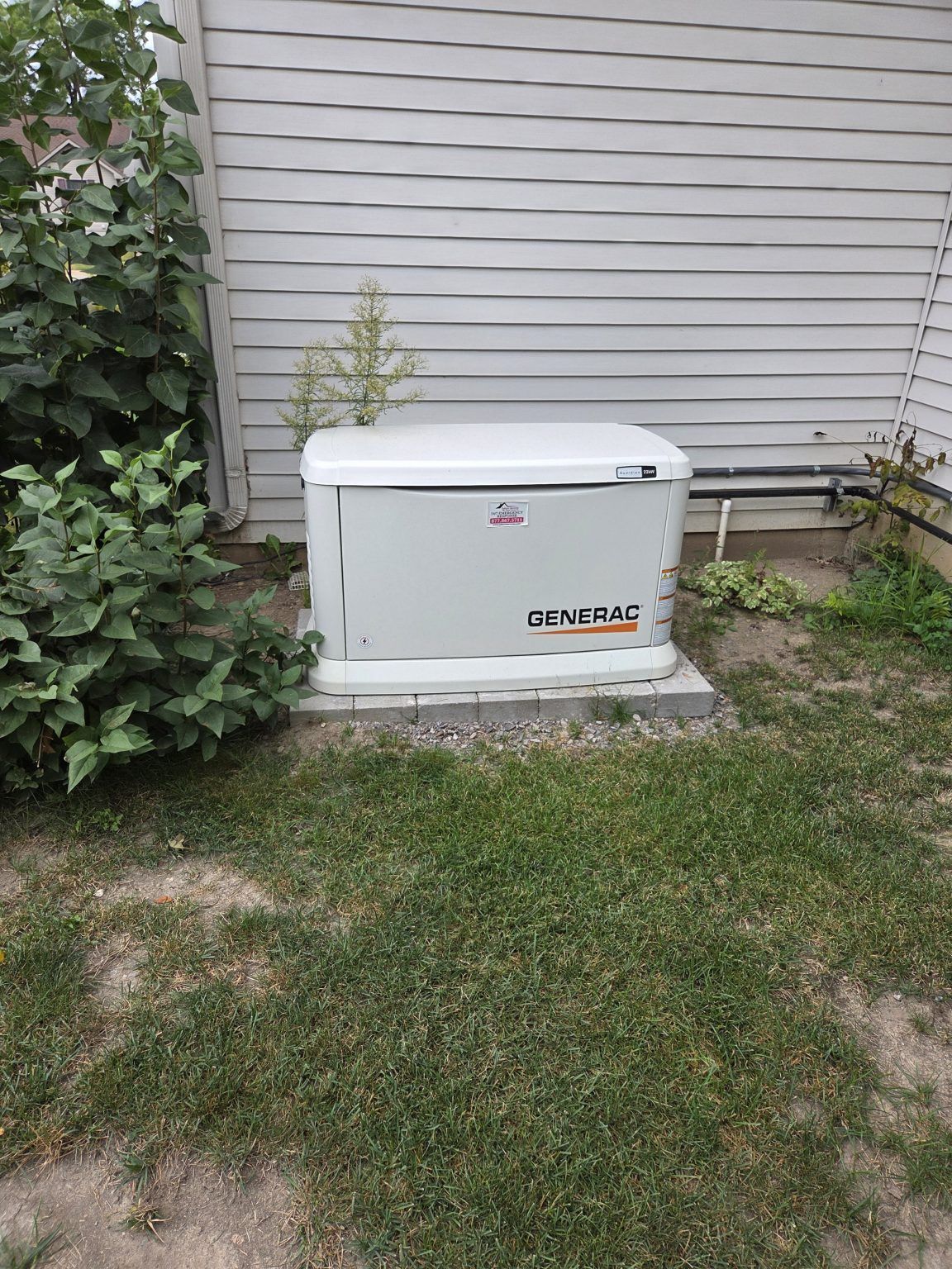 Gray Generac home generator on a concrete pad near a house.