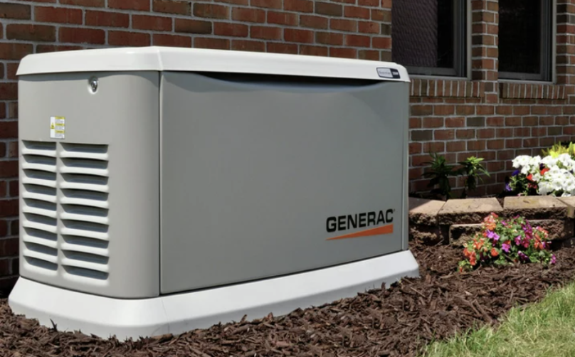 Gray Generac home standby generator next to a brick wall and flowerbed.