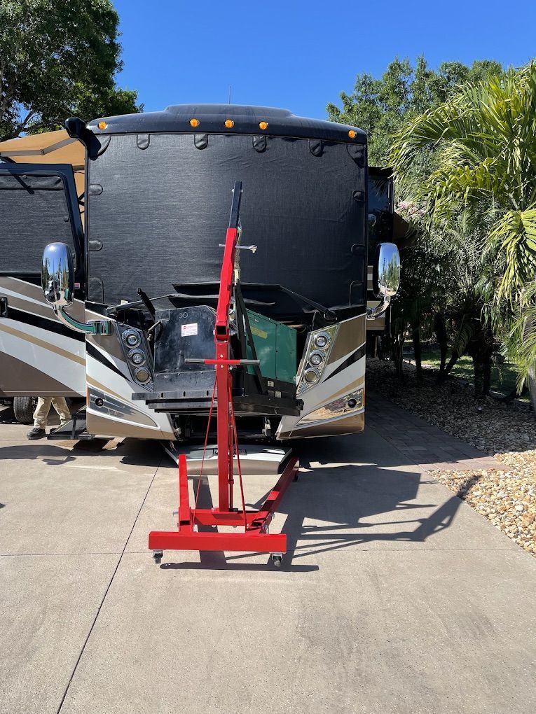 Red engine hoist in front of a parked RV; sunny outdoor setting.