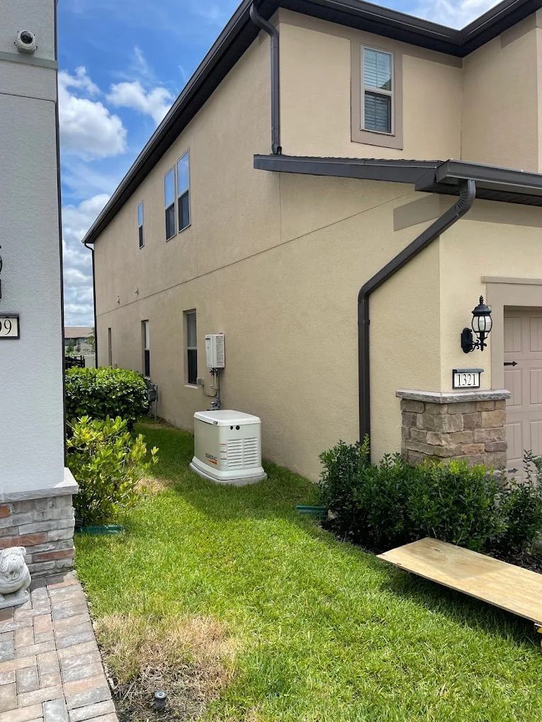 Side view of a two-story beige house with a backup generator in the grass.