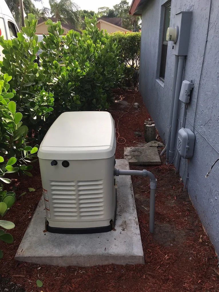 Generator on concrete pad next to a house with electrical components. Surrounded by mulch and bushes.