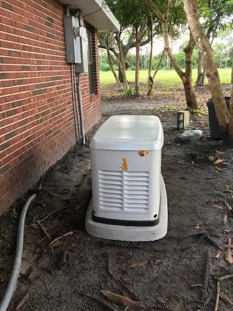 Generator unit near a brick house, on a concrete pad, outdoors.
